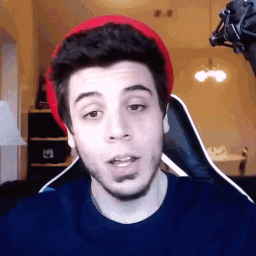 a man wearing a red hat is sitting in front of a microphone making a funny face