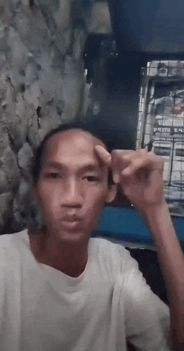 a man in a white shirt is making a funny face while holding his hand to his forehead .
