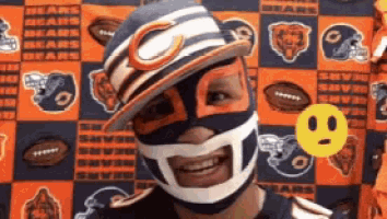 a man wearing a bears hat and mask smiles in front of a bears background