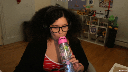 a woman wearing glasses and headphones is drinking from a pink bottle that says shagarita on the top