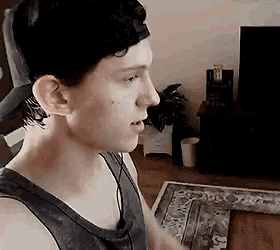 a young man wearing a tank top and a baseball cap is standing in a living room .