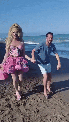 a woman in a pink dress is holding hands with a man on the beach