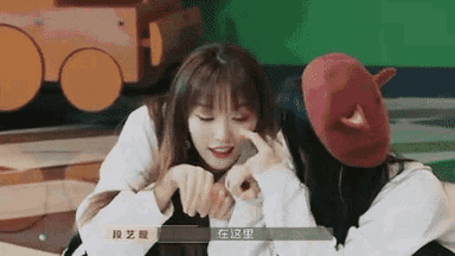 two girls are sitting next to each other and one is pointing at the other 's nose .