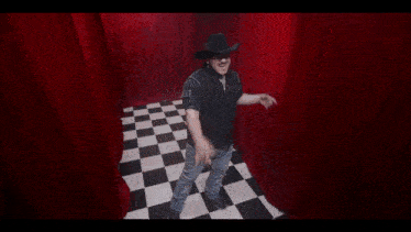 a woman in a white dress is kneeling down on a checkered floor in a room with red curtains .