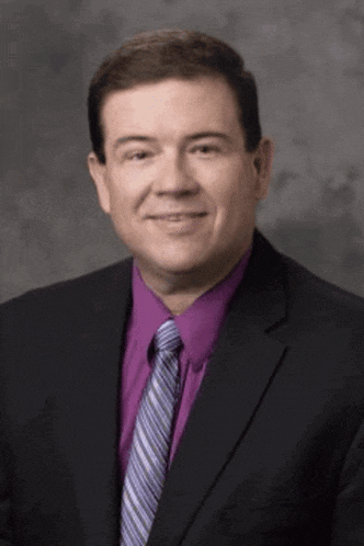 a man in a suit and purple shirt is smiling