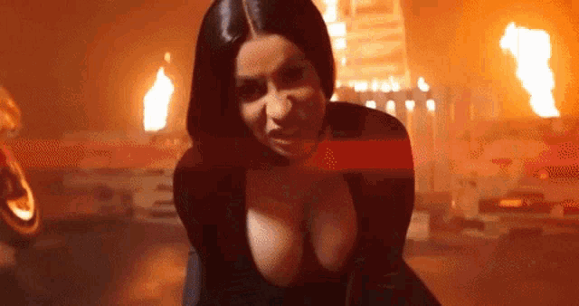 a woman in a black dress is standing in front of a fire in a dark room .