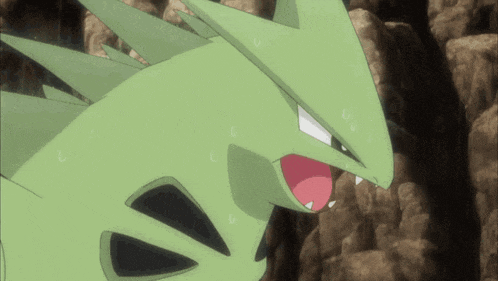 a green pokemon with a red tongue is standing on a rocky hillside