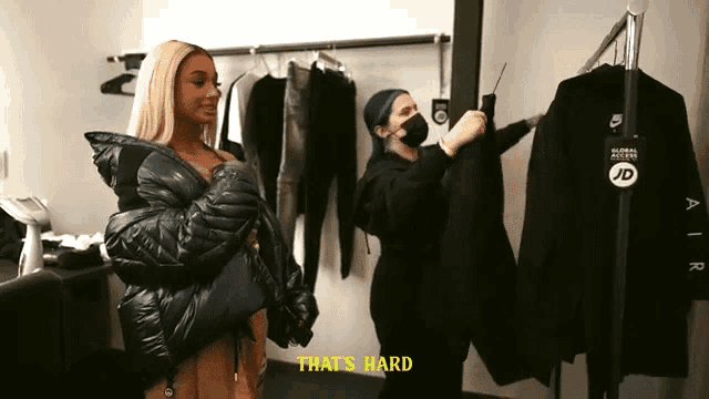 a woman in a black jacket is standing next to a woman in a mask and the words that 's hard are visible