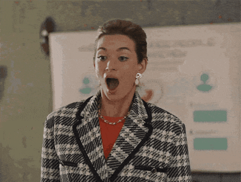a woman in a plaid jacket is making a surprised face in front of a whiteboard