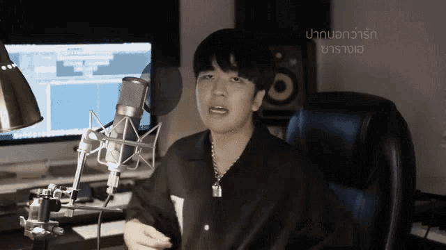 a man sitting in front of a microphone with the words " ปาก บอก ว่า รัก " on the bottom
