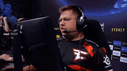 a man wearing headphones and a shirt with the letter f on it sits in front of a monitor