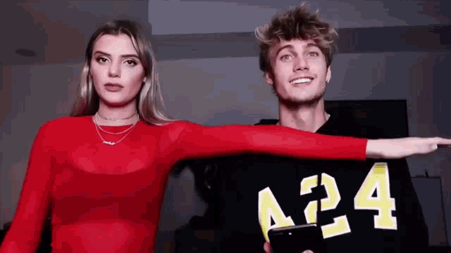 a man and a woman are standing next to each other and the man is wearing a sweater that says a24 on it