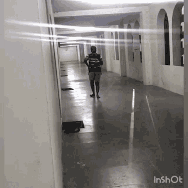 a man is walking down a hallway with the words inshot on the bottom right