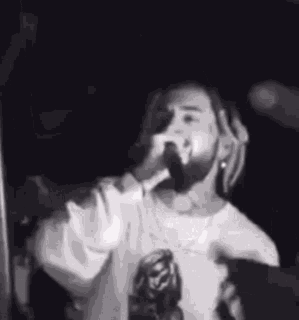 a man with dreadlocks is singing into a microphone on a stage in a black and white photo .