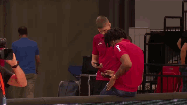 a man in a red shirt is talking to another man in a black shirt