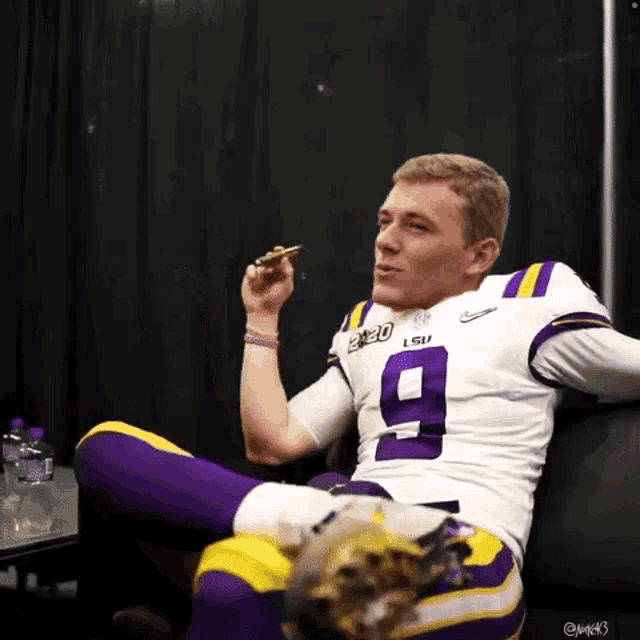 a man in a lsu jersey sits on a couch smoking a cigar