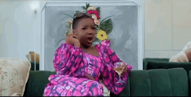 a woman in a pink dress is sitting on a green couch with a glass of wine .