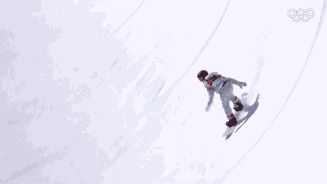 a snowboarder is riding down a snow covered slope with the olympics logo in the background