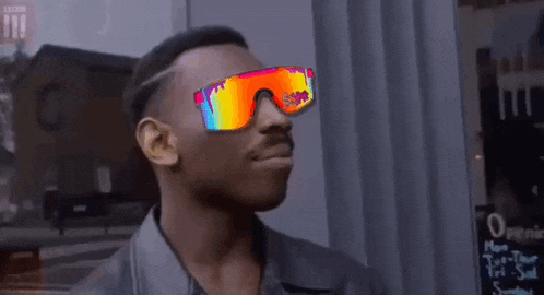 a man wearing sunglasses is standing in front of a building and making a funny face .