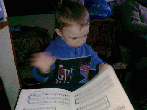 a young boy wearing a spider-man shirt is reading a sheet music