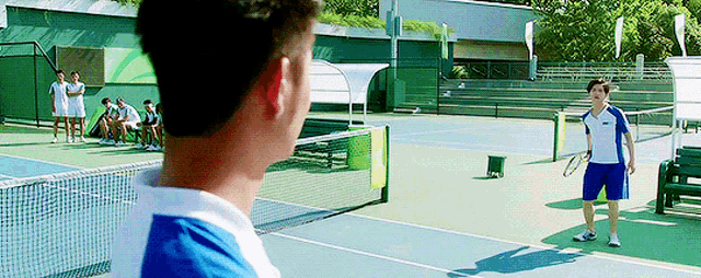 a man is standing on a tennis court looking at another man holding a tennis racket .