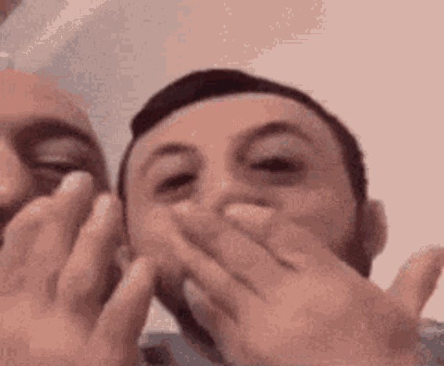 two men are covering their mouths with their hands while looking at the camera .