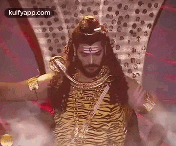 a man with long hair and a beard is dressed as a tiger and holding a snake .