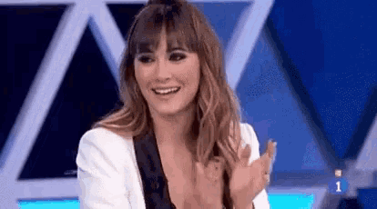 a woman is smiling and clapping her hands while sitting on a stage in front of a blue background .