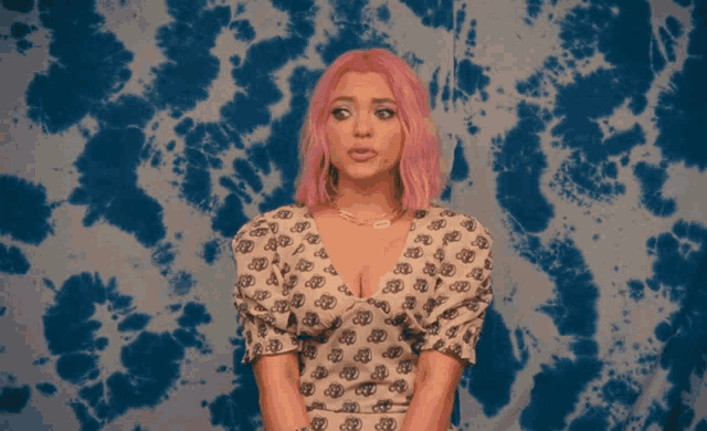 a woman with pink hair is standing in front of a blue tie dye background
