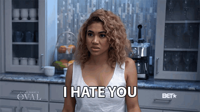 a woman in a white tank top says i hate you in a kitchen