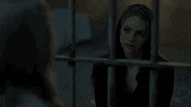 a woman is behind bars in a jail cell and looking out the window .