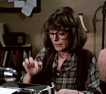 a woman wearing glasses sits at a desk with a typewriter