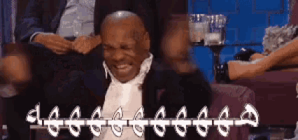 a man in a suit and tie is sitting on a couch with his hands in the air .
