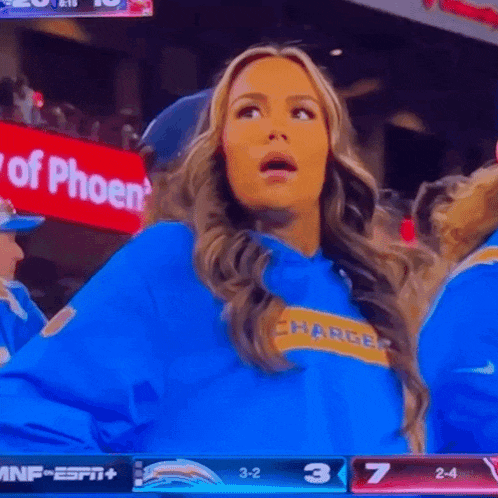 a woman wearing a blue chargers shirt is watching a football game