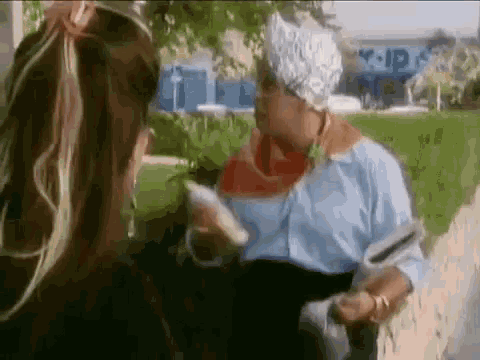 a woman is talking to a man wearing a tin foil hat while holding a newspaper .