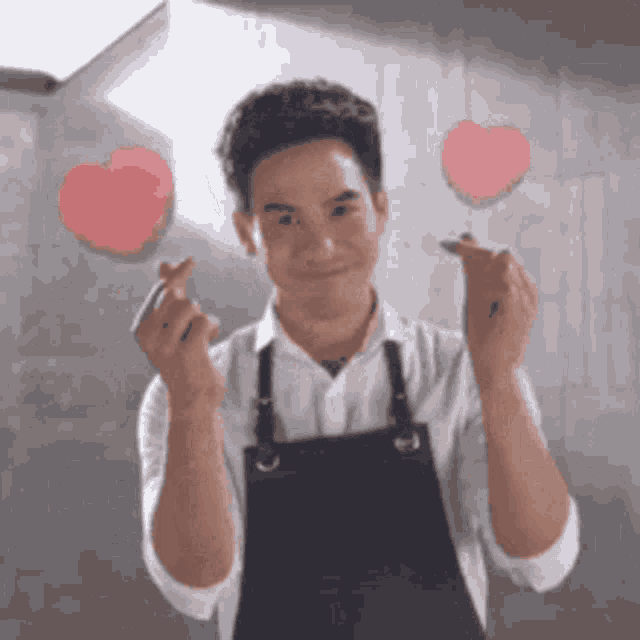 a man wearing an apron is making a heart with his hands .