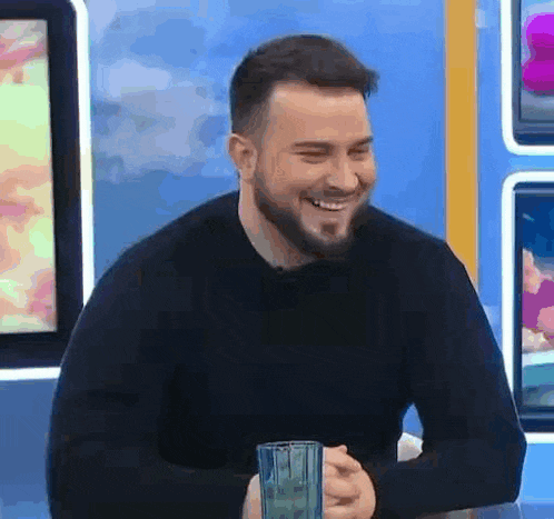 a man with a beard is smiling and holding a glass of water .