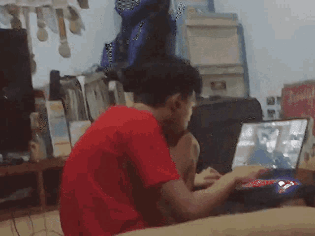 a man in a red shirt is playing a game on a laptop