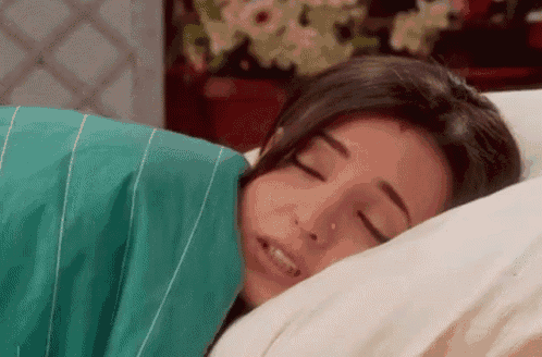 a woman is sleeping on a bed with her eyes closed and a green blanket .