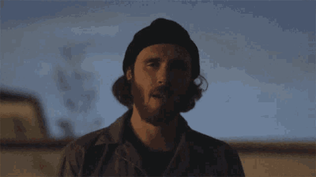 a man with a beard wearing a beanie looks down