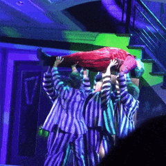a group of people in striped pajamas are carrying a person in a red suit on their shoulders