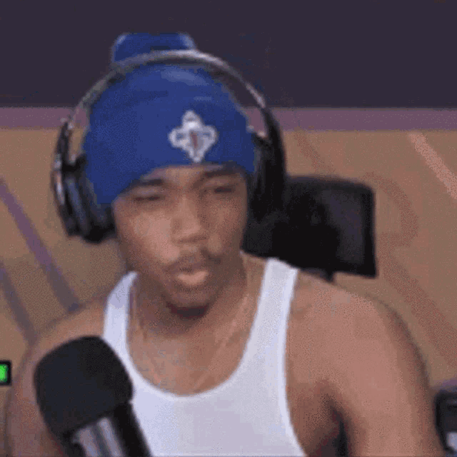 a man wearing a blue hat and headphones is talking into a microphone .