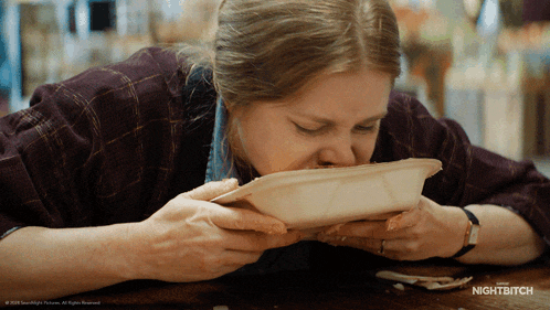 a woman is eating from a styrofoam container with nightbitch written on the bottom of the image