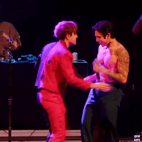 two men are hugging each other on a stage and one of them has a tattoo on his arm