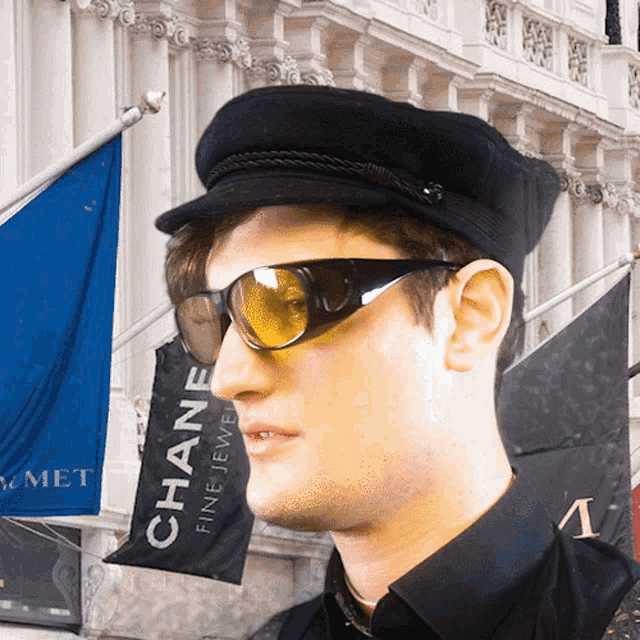 a man wearing sunglasses and a black hat stands in front of a banner that says chane fine jewelry