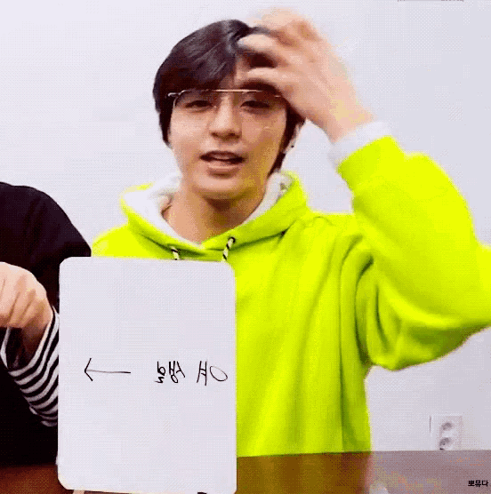 a young man wearing glasses and a neon yellow hoodie is holding a white card with chinese writing on it .
