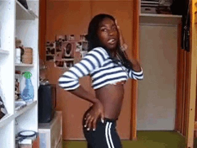 a woman is standing in a room wearing a striped crop top and black pants .