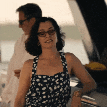 a woman wearing glasses and a polka dot dress is standing next to a man on a boat