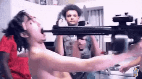 a man without a shirt is holding a gun in a kitchen .