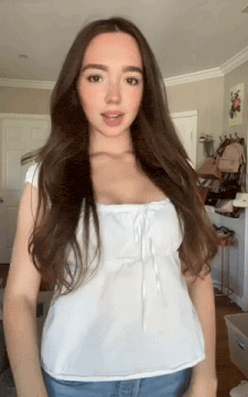 a woman with long brown hair wearing a white top and blue jeans